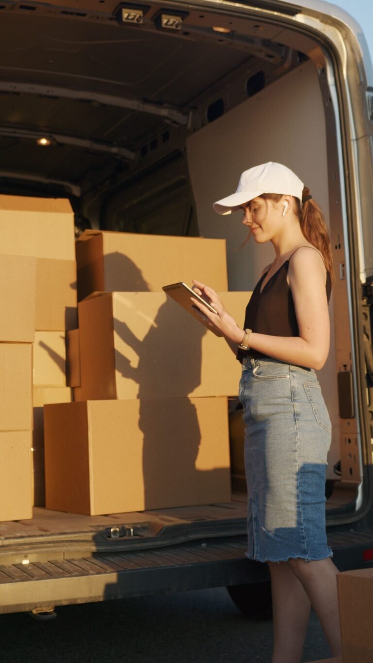 Young female courier organizing package delivery beside an open delivery van at sunset.